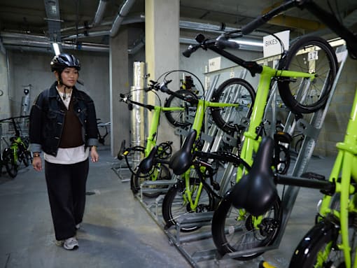 A woman in a helmet is walking past a row of green bicycles.