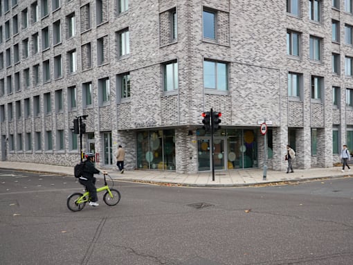 A person riding a bicycle in front of a grey building.