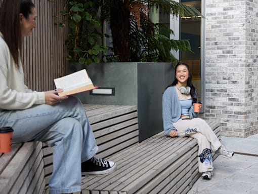 Two people sitting on a bench, one reading a book.