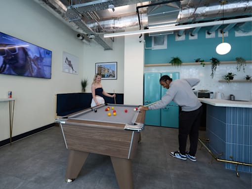Two people playing pool in a room with a pool table.