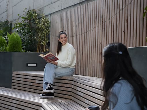 A woman is sitting on a bench reading a book.