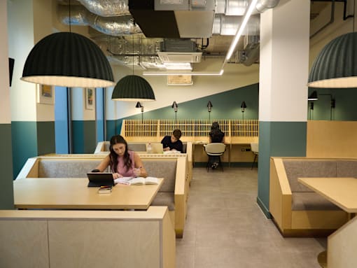 A woman is studying at a table in a library with a laptop and books.