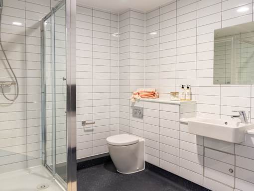 A white tiled bathroom with a toilet, sink, and shower.