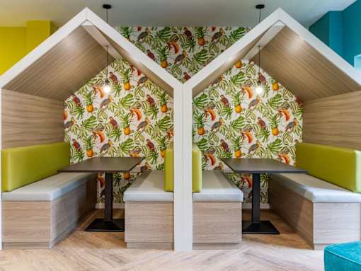 Two booths with a fruit patterned wallpaper and green cushions.