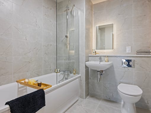 A bathroom with a white toilet, a white sink, and a white bathtub with a tray of soaps and a black towel.