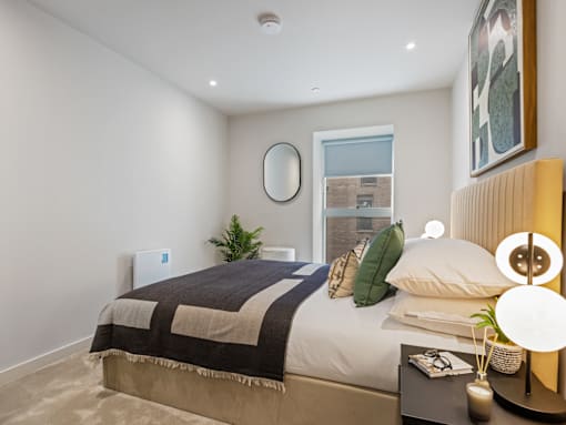 A bedroom with a bed, a mirror, a plant, and a framed picture on the wall.