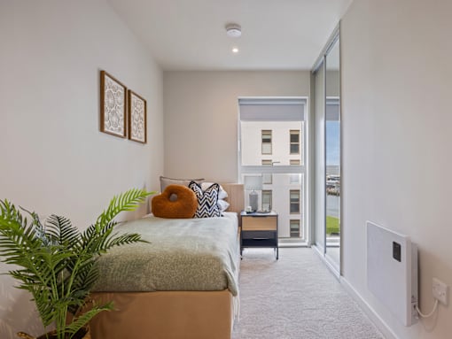 A bedroom with a bed, a plant, and a window.