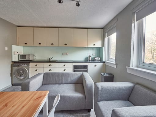 A modern kitchen with a grey couch and a wooden table.