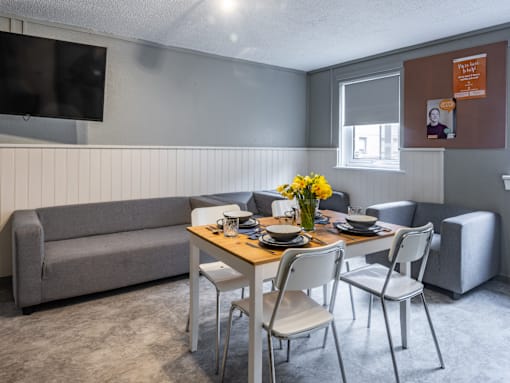 A grey couch sits in a room with a table and chairs.