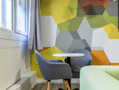 A dining table with two grey chairs in front of a wall with a geometric pattern.
