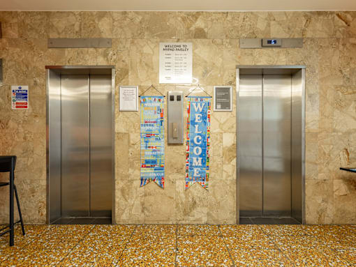 Two elevators flank a wall with a sign that says "Welcome towel.".