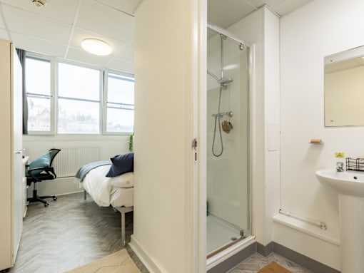 A small bedroom with a bed, chair, and shower.