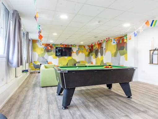 A pool table is in the middle of a room with a TV and a green chair.