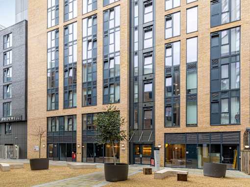 A modern building with a black and brown facade and a courtyard with trees and benches.