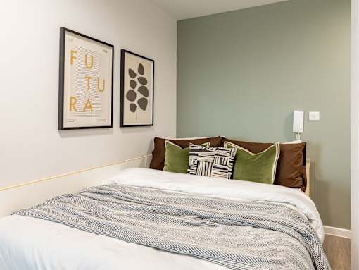 A bedroom with a bed, pillows, and two framed pictures on the wall.