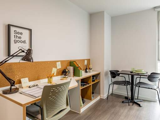 A room with a desk, chairs, and a corkboard with a sign that says "See the good.".