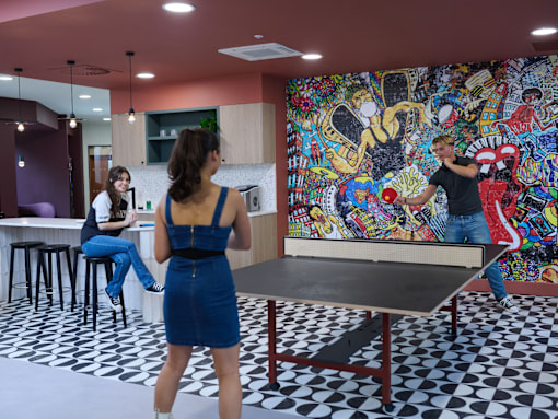 A woman in a blue dress is playing ping pong in a room with a colorful mural on the wall.