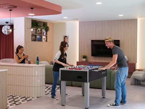 A man and two women are playing a game of foosball in a modern room.