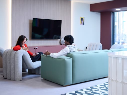 Two people sitting on a couch in a room with a television and a window.