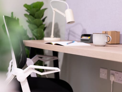 A white desk with a laptop, a cup, a book, a pen, a lamp, and a plant.