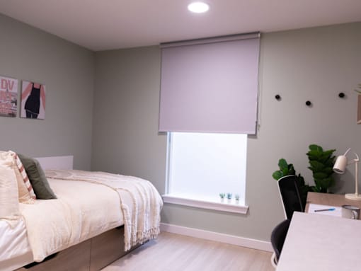 A bedroom with a bed, desk, and window with blinds.