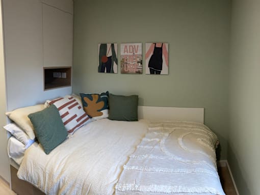 A white bed with a white headboard and a white comforter with a white pillow and a green pillow.