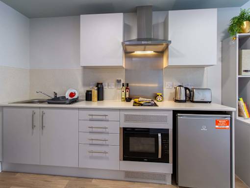 A White studio kitchen space with an oven, fridge, hobs, extractor fan, cupboards and drawers.