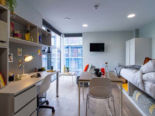 A bedroom with a white desk with a chair and a small dining table with 2x chairs.