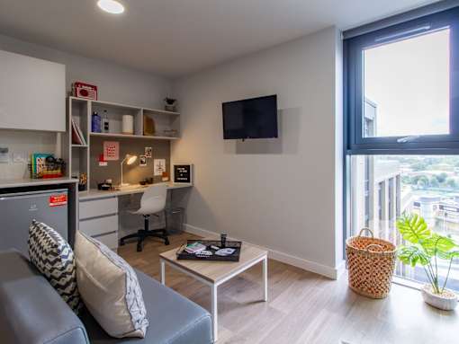 Room with a grey couch, small coffee table, wall-mounted TV and a desk with a desk chair.