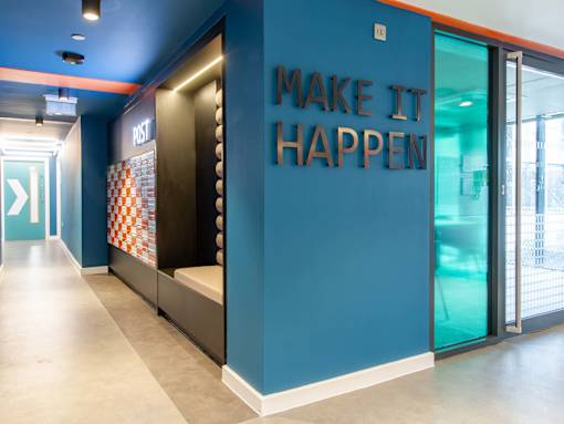 Positive wall-art stating 'Make It Happen' against a blue wall, near to the reception.