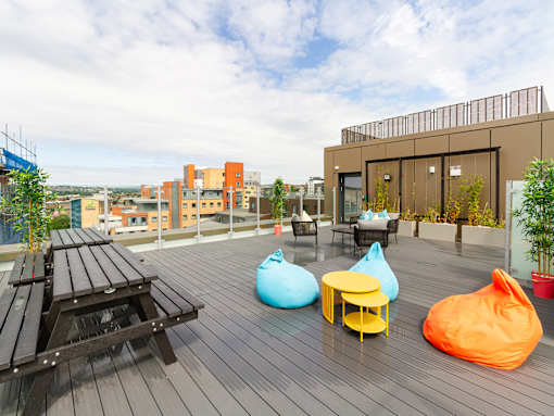 A modern roof-top patio with bean bags and a wooden bench.