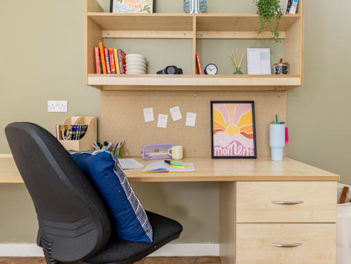 A home office with a desk, chair, and shelf with various items.