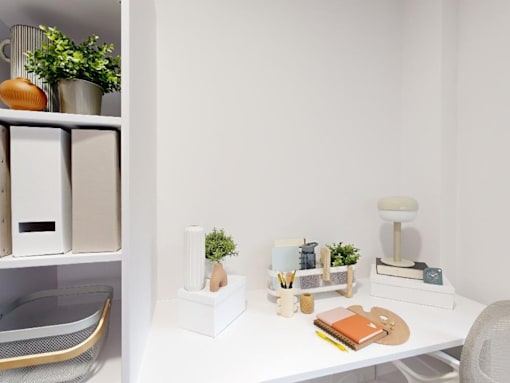 A white desk with a chair, a plant, and some stationery items.