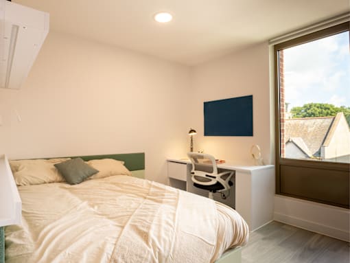 A bedroom with a bed, desk, and window.