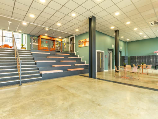 the lobby of a building with a staircase and tables and chairs