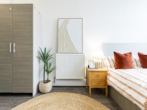 A bedroom with a bed, nightstand, and a plant.