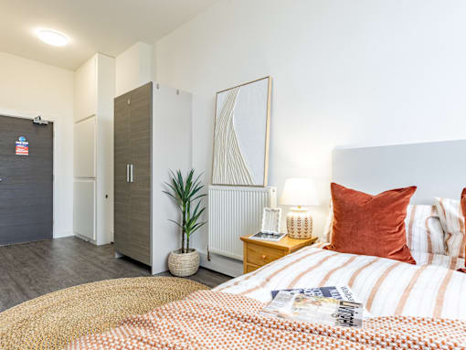 A bedroom with a bed, nightstand, and a plant.