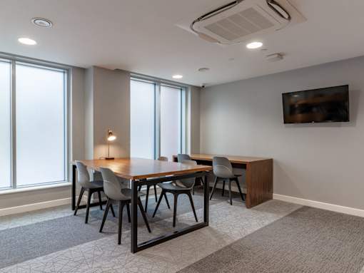 A conference room with a long table and chairs, a television on the wall, and a carpeted floor.