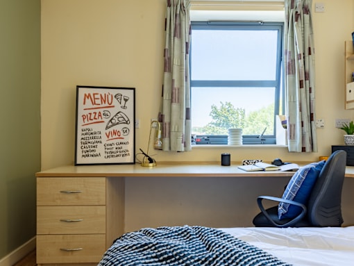 A room with a bed, desk, and a menu board on the wall.