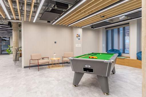 A room with a pool table and chairs.
