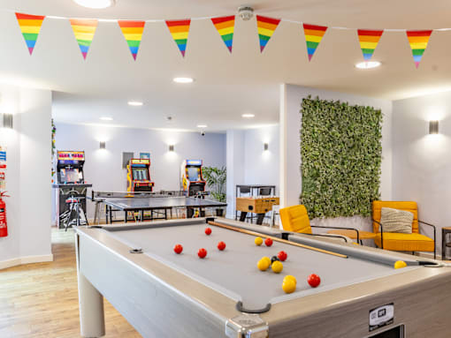 A pool table is in the middle of a room with a green wall and a fire extinguisher on the wall.
