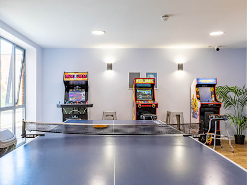A ping pong table is in the middle of a room with arcade games on the wall.