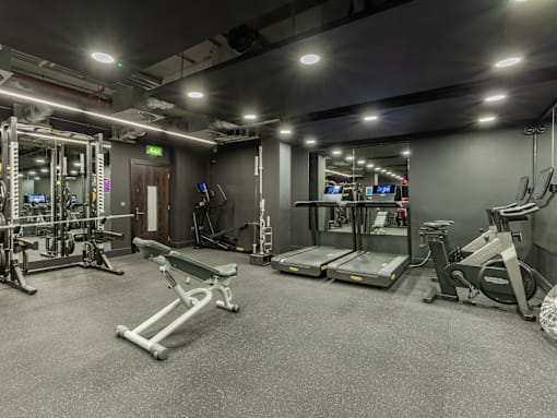 A gym with a variety of equipment including treadmills, weight machines, and a bench press.