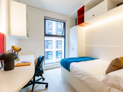 A bedroom with a bed, desk, chair, and window.