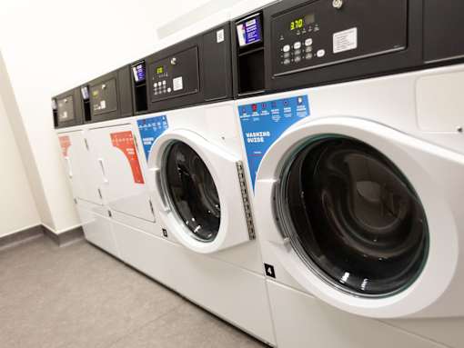 A row of washing machines with the front left one having a blue sticker on it.