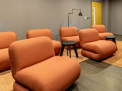 A row of orange chairs with black stools in front of them.