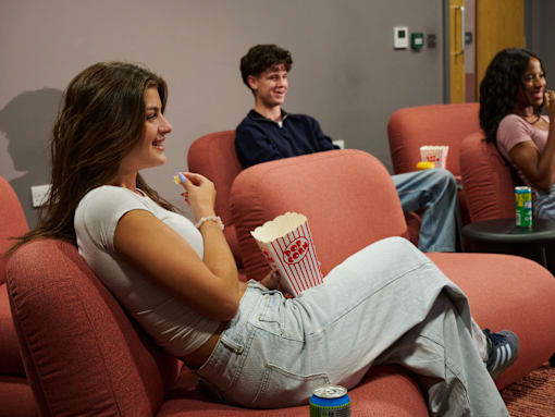 A woman is sitting on a red couch eating popcorn.