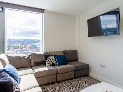 A living room with a brown couch and a flat screen TV mounted on the wall.