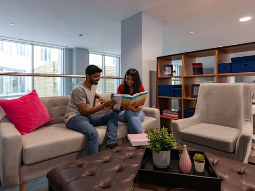 Two people sitting on a couch reading a book in a living room.