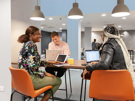 Three people are sitting around a table with laptops.